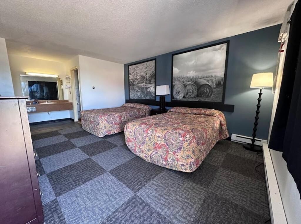 A hotel room with two beds, a flat-screen TV, a desk, and a lamp.