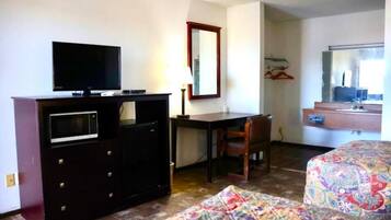 Una habitación de hotel con una cama, un escritorio con televisor, un aparador, una silla y un espejo.