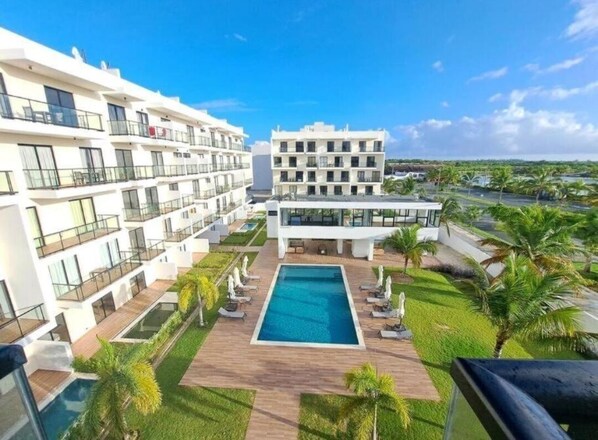 A modern hotel with a central pool, multiple balconies, and a view of the surrounding landscape.