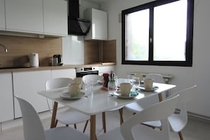 A modern kitchen with white cabinets, a dining table set with cups and saucers, and a window with blinds.