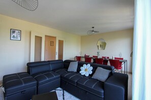 Un salon avec un canapé d’angle, une table à manger avec des chaises rouges et un ventilateur de plafond.