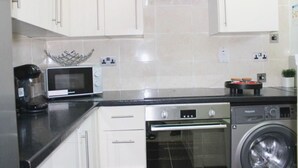 Una cocina con gabinetes blancos, microondas, cafetera, lavavajillas y lavadora.