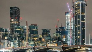 Un paisaje urbano nocturno con edificios modernos y un puente sobre un cuerpo de agua.