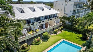 A multi-story hotel with a swimming pool, surrounded by well-maintained lawns and palm trees.