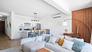 A modern living room with a sectional sofa, a wooden coffee table, and a dining area with a kitchen in the background.