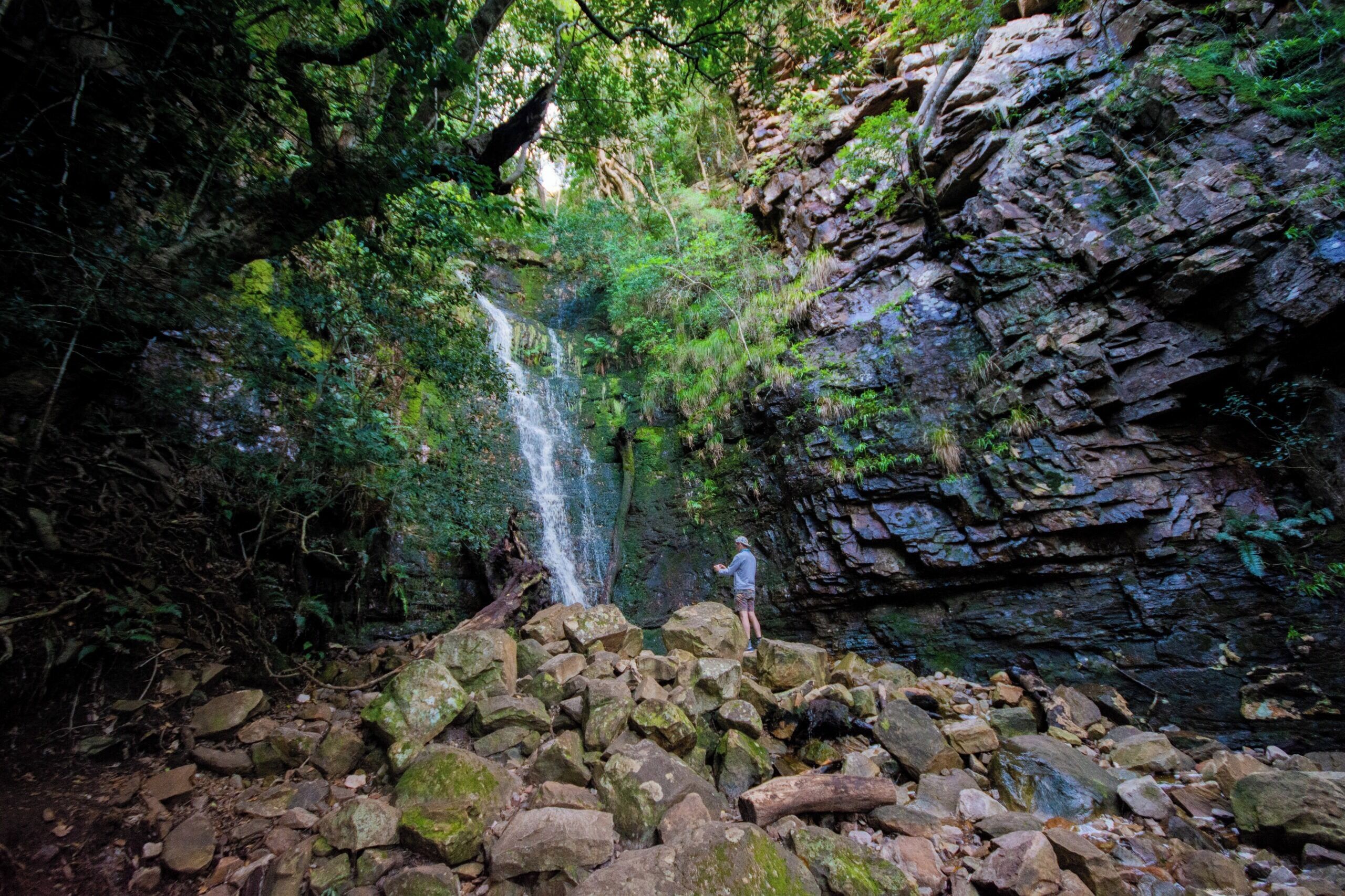 A natural waterfall surrounded by rocks and dense foliage.