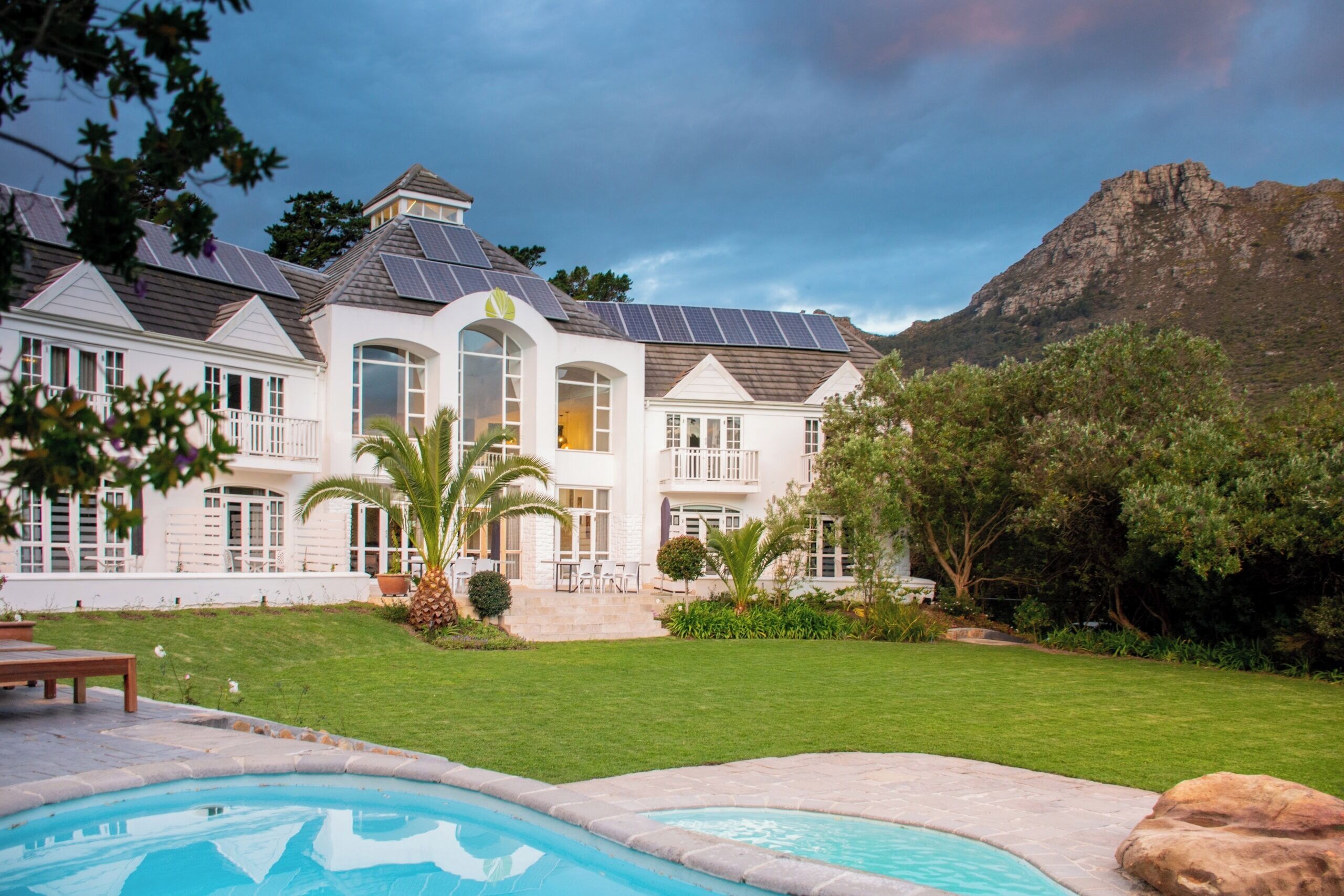 Une grande maison moderne dotée d’une piscine, entourée d’une végétation luxuriante et avec une chaîne de montagnes en toile de fond.