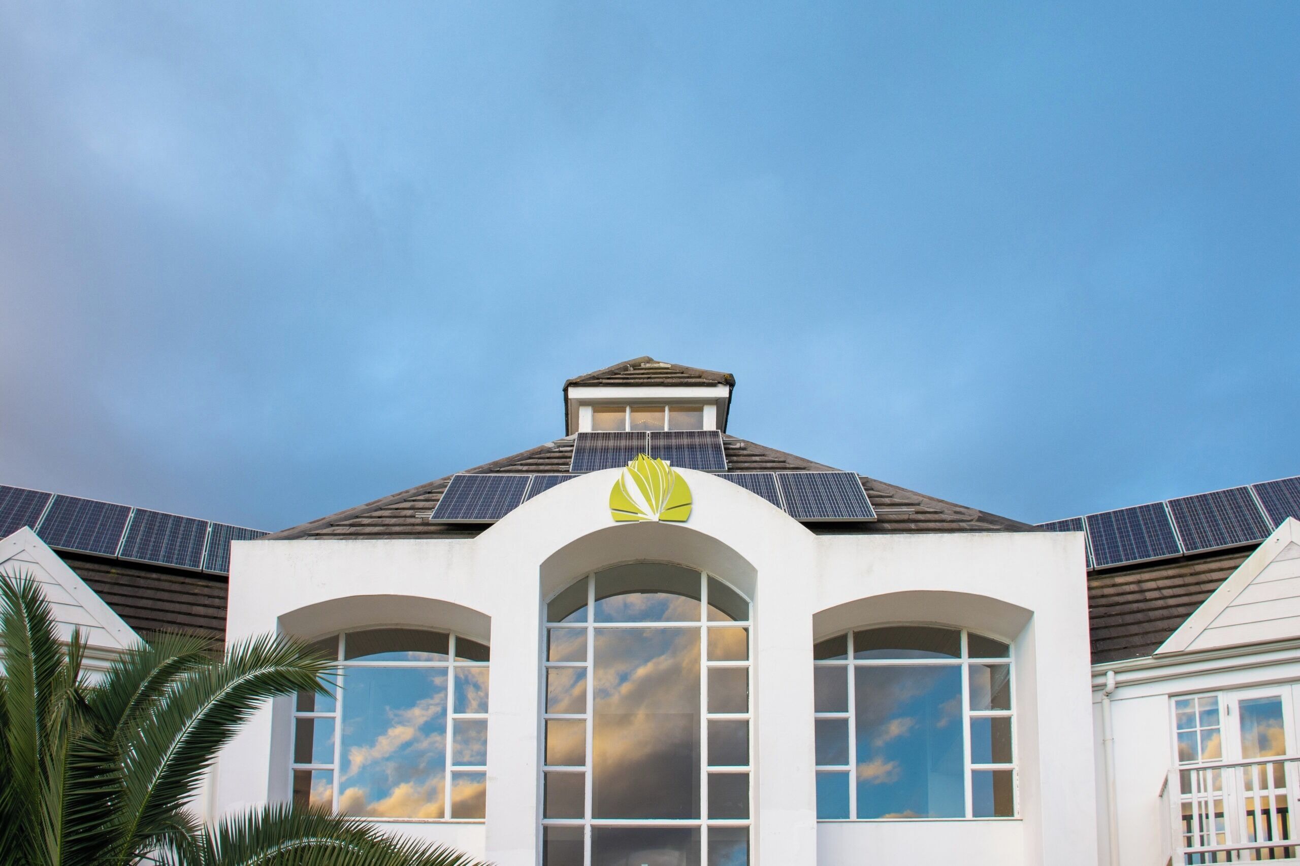 A building with a white facade, arched windows, and a green logo on the roof.