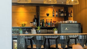 Un espace bar agrémenté de trois lampes suspendues, d’un comptoir avec des bouteilles et des verres, ainsi que de plusieurs chaises et tables.
