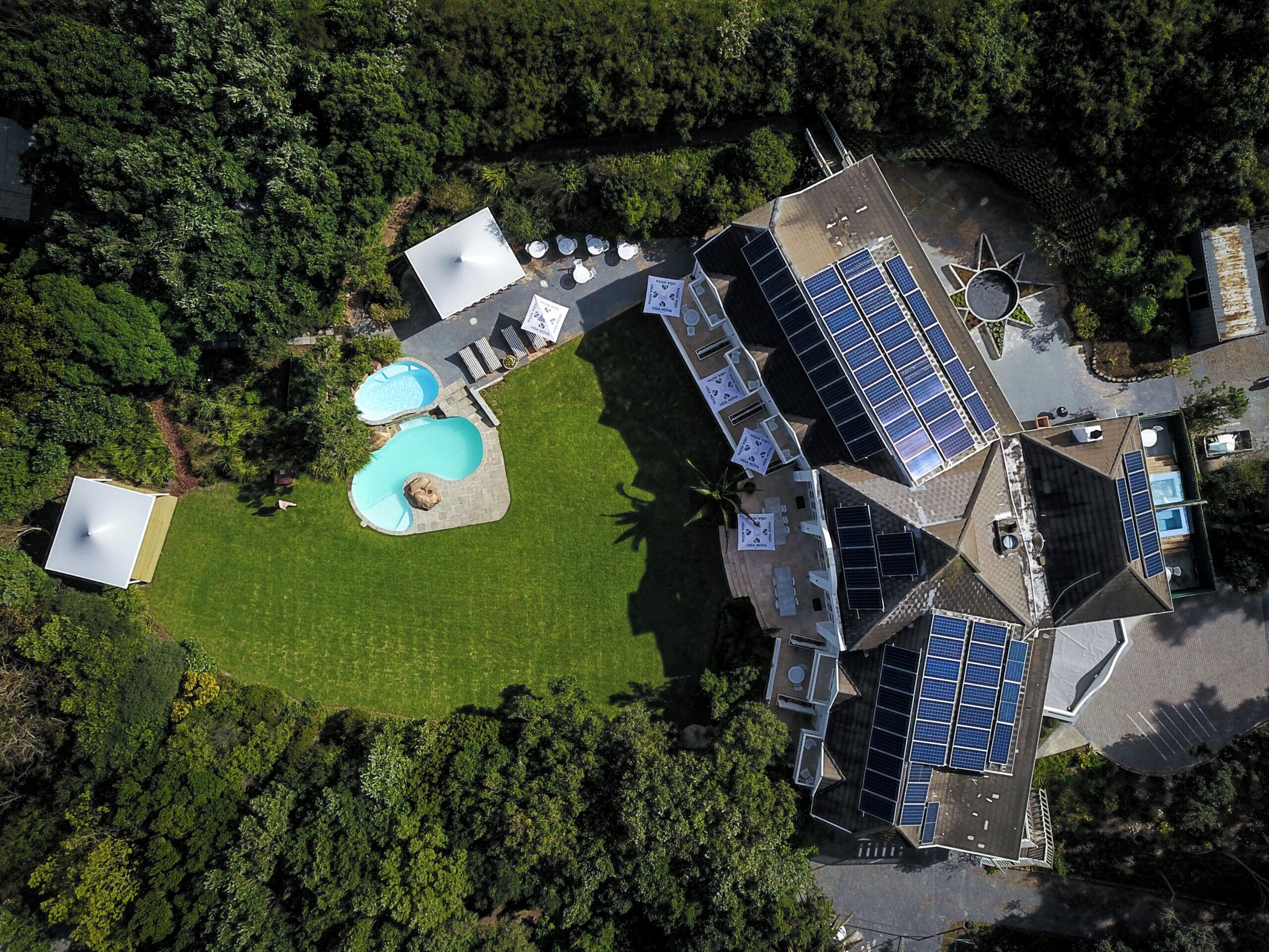 Vista aérea de una propiedad con piscina, paneles solares y un césped bien cuidado.