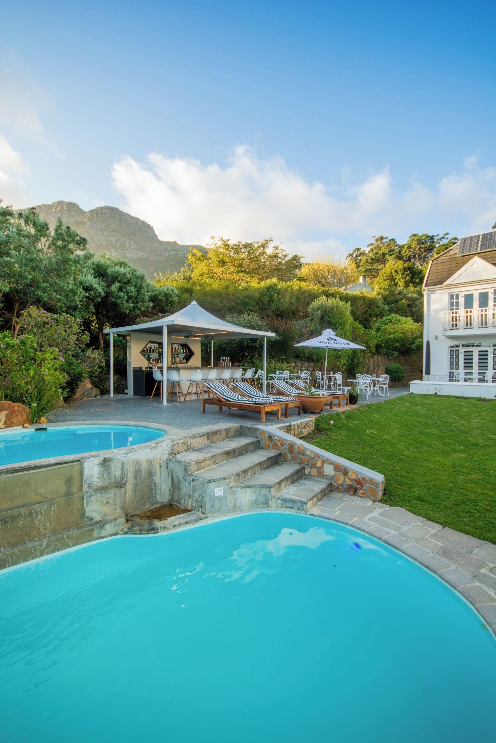 A pool area with a bar and lounge chairs, surrounded by a well-maintained lawn and a mountain in the background.