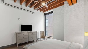 A bedroom with a bed, a TV on a dresser, a chair, and a large window. - Amazing Riverfront Views - Steps from Arch (St. Louis)