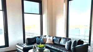 A modern living room with a sectional sofa, a coffee table with a plant, and large windows offering a view of a waterfront. - Amazing Riverfront Views - Steps from Arch (St. Louis)