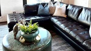 A modern living room with a black leather sectional sofa, a round coffee table with a plant, and a large window offering a view of a bridge. - Amazing Riverfront Views - Steps from Arch (St. Louis)