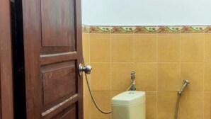A bathroom with a wooden door, a toilet, and tiled walls. - Backpacker Homestay (Sumberagung)