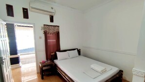 A bedroom with a bed, a nightstand, an air conditioning unit, a window with curtains, and a door leading outside. - Backpacker Homestay (Sumberagung)