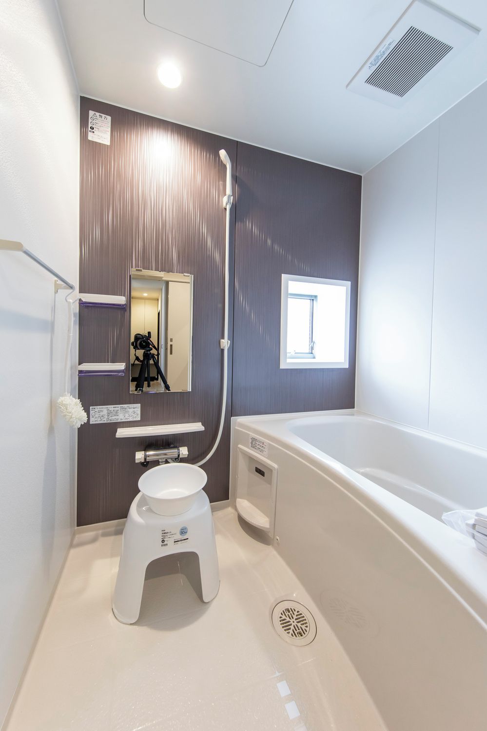 A modern bathroom with a bathtub, a small stool, a mirror, and a window.