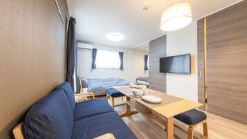 A modern, compact room with a sofa, a dining table, and a TV mounted on the wall.