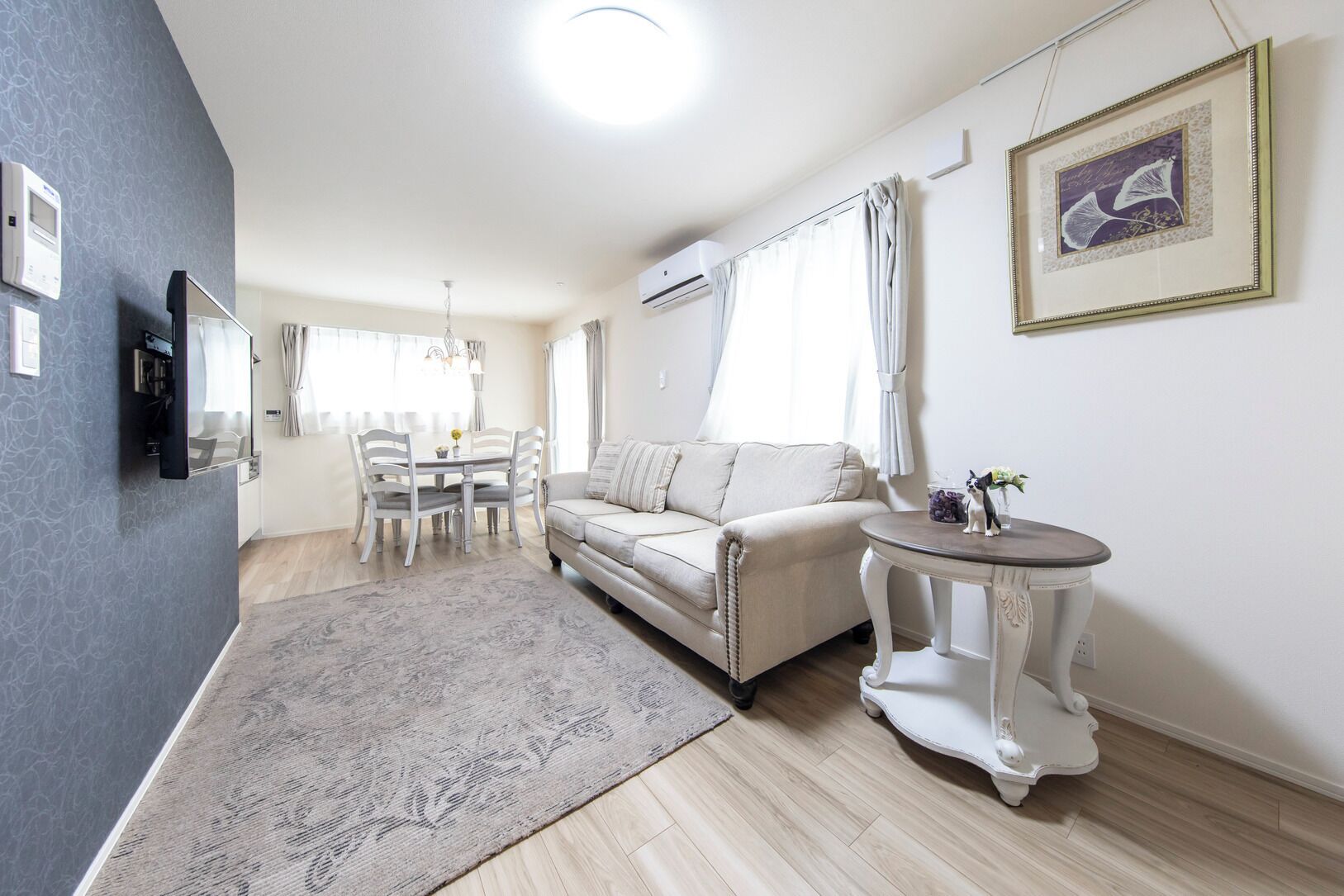 Una sala de estar moderna con un sofá, una mesa de comedor con sillas, una pequeña mesa redonda con un florero y un cuadro en la pared.