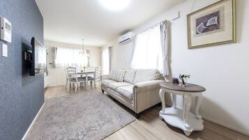 Una sala de estar moderna con un sofá, una mesa de comedor con sillas, una pequeña mesa redonda con un florero y un cuadro en la pared.