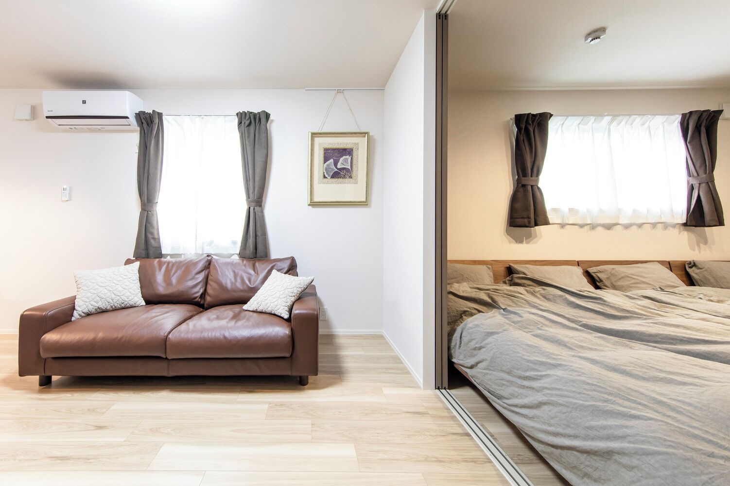 Uma sala de estar moderna com um sofá de couro marrom, um quadro na parede e uma cama com roupa de cama cinzenta.