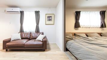 Uma sala de estar moderna com um sofá de couro marrom, um quadro na parede e uma cama com roupa de cama cinzenta.