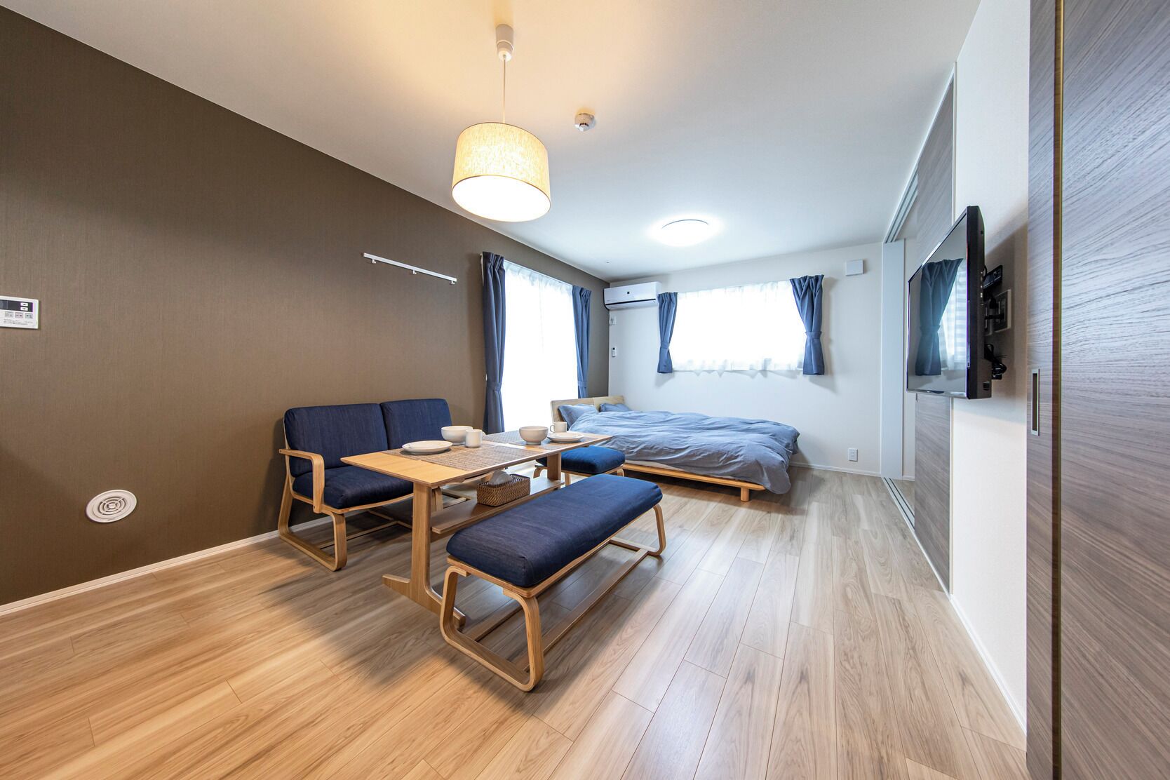 A compact room with a bed, a sofa, a dining table, and a TV.