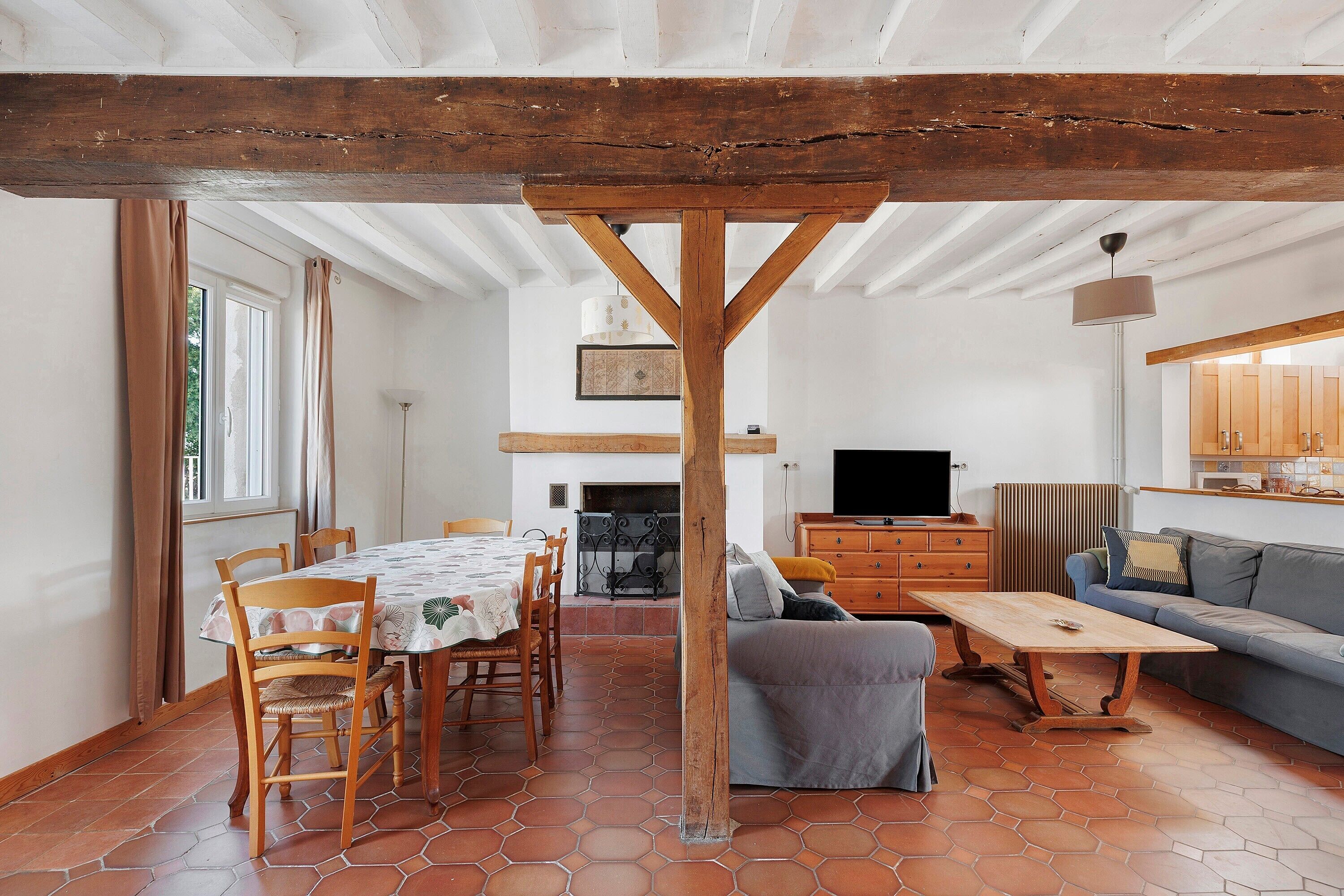 A dining area with a wooden table and chairs, a sofa, and a television in a living room.