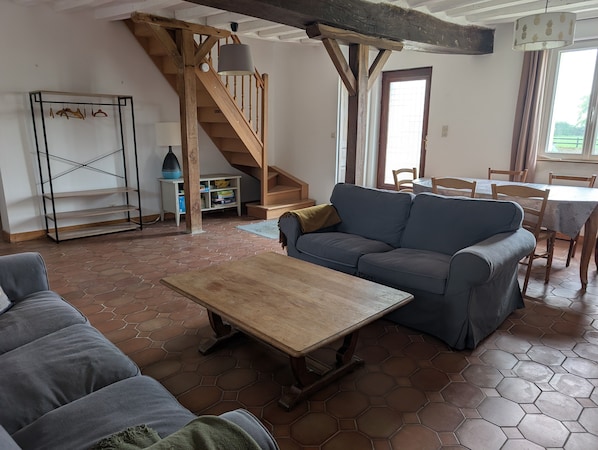 Una sala de estar con sofá, una mesa de centro de madera, una escalera y un comedor.