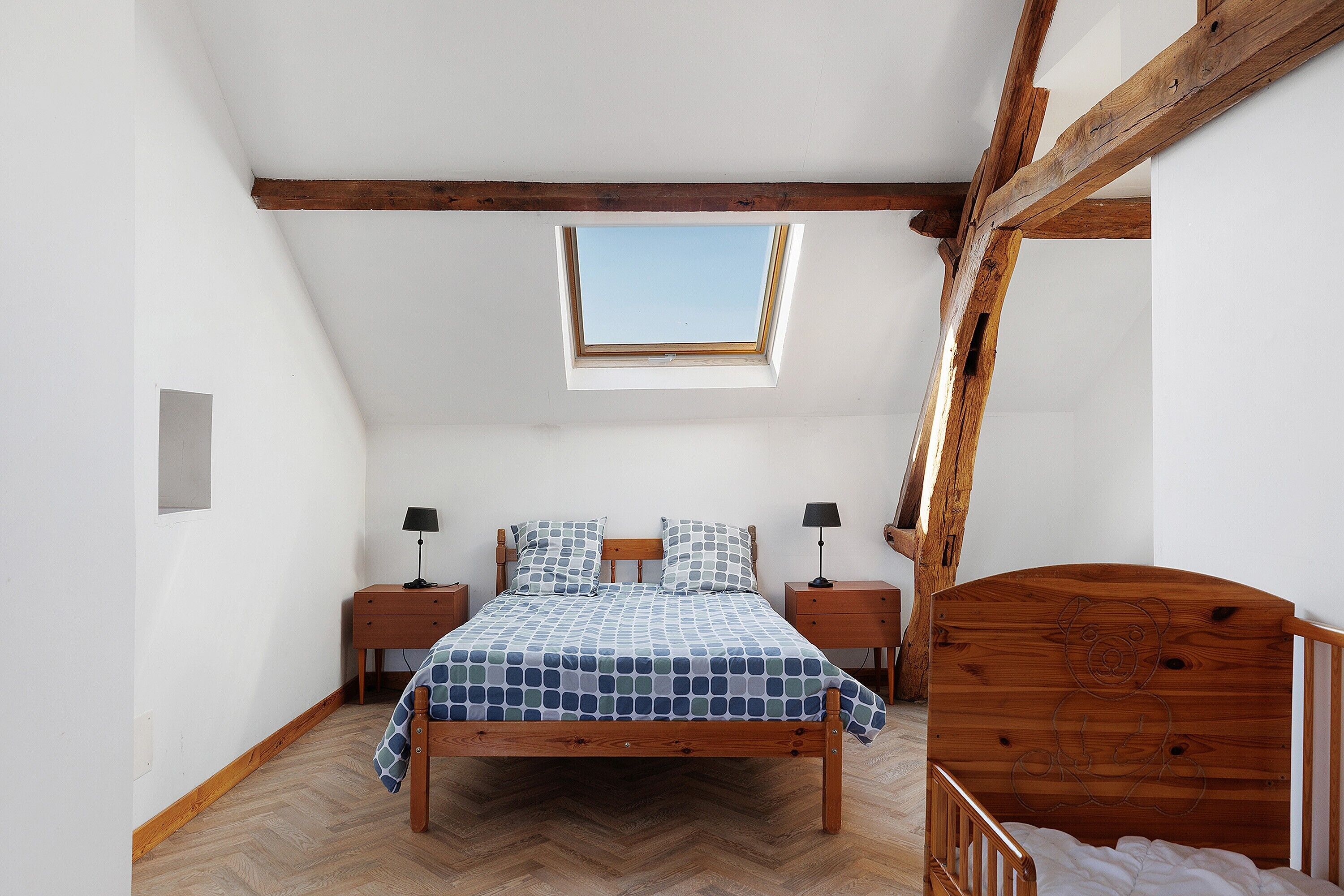 Een slaapkamer met een houten bed, dakraam, houten hoofdbord en een visgraat vloer.