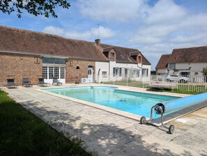 Una piscina con sillones de descanso, un edificio de ladrillo y una cerca blanca.