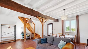 Ein Wohnzimmer mit Holztreppe, einer Couch, einem Couchtisch und einem Essbereich mit Tisch und Stühlen.