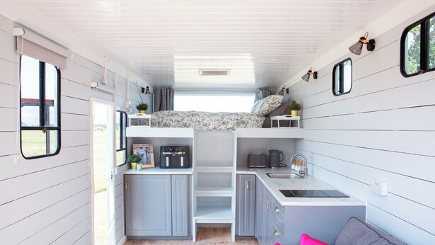 A compact kitchen with a built-in stove, a sink, and a small countertop. There is a window above the sink and a door on the left side.