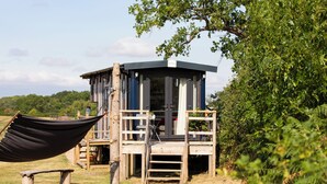 A wooden structure with a balcony, a hammock, and a bench in a natural setting.