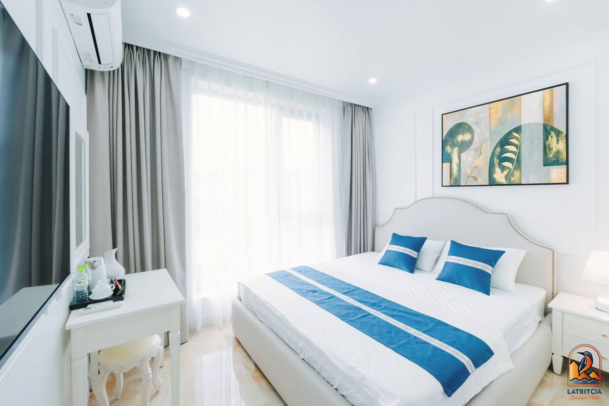 A hotel room with a large bed, a desk with a chair, a TV, and a window with curtains.