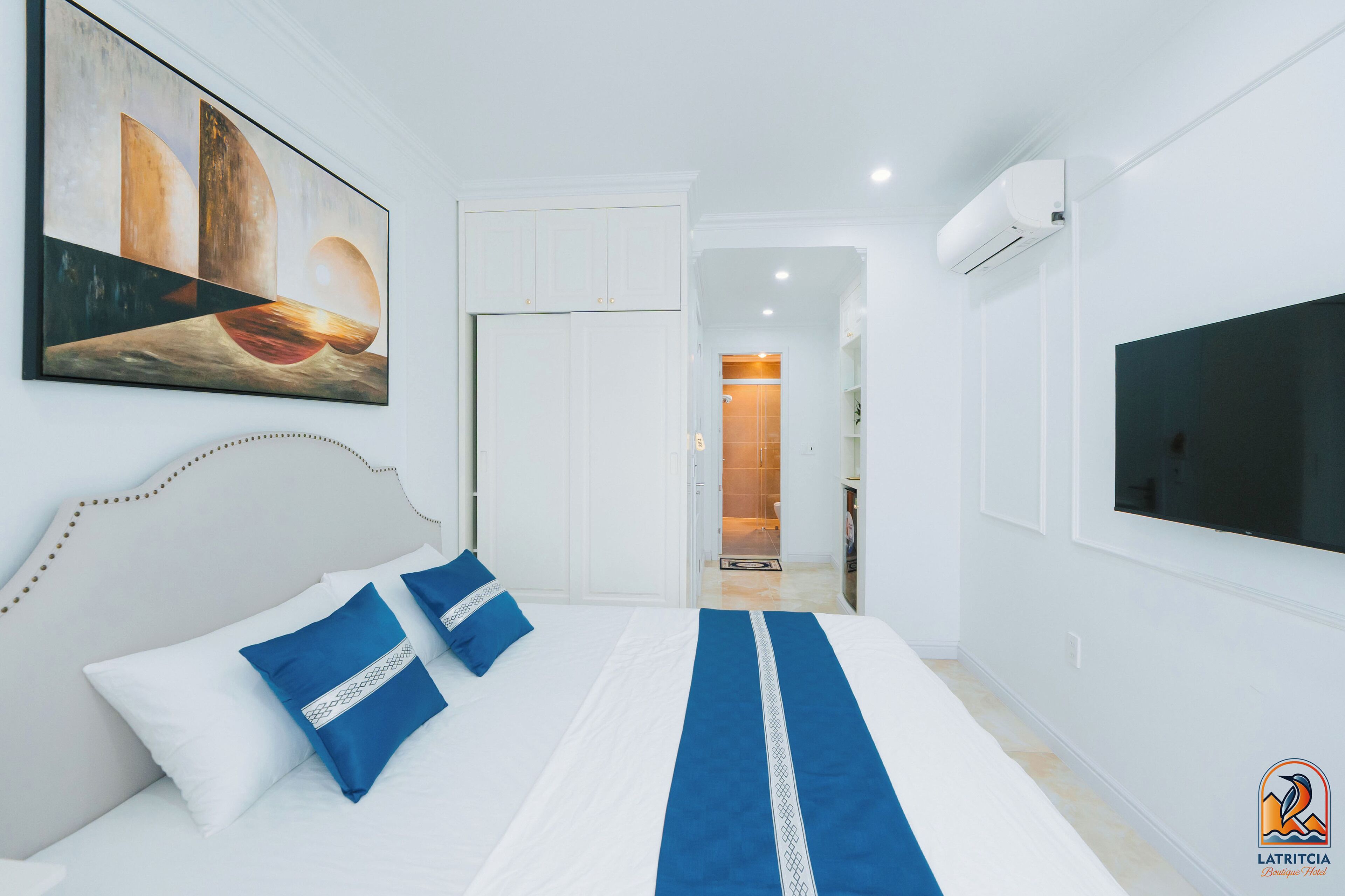 Habitación de hotel con una cama, un cuadro, un televisor y un baño visible a través de una puerta abierta.