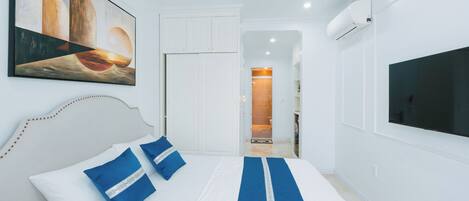 A hotel room with a bed, a painting, a TV, and a bathroom visible through an open door.