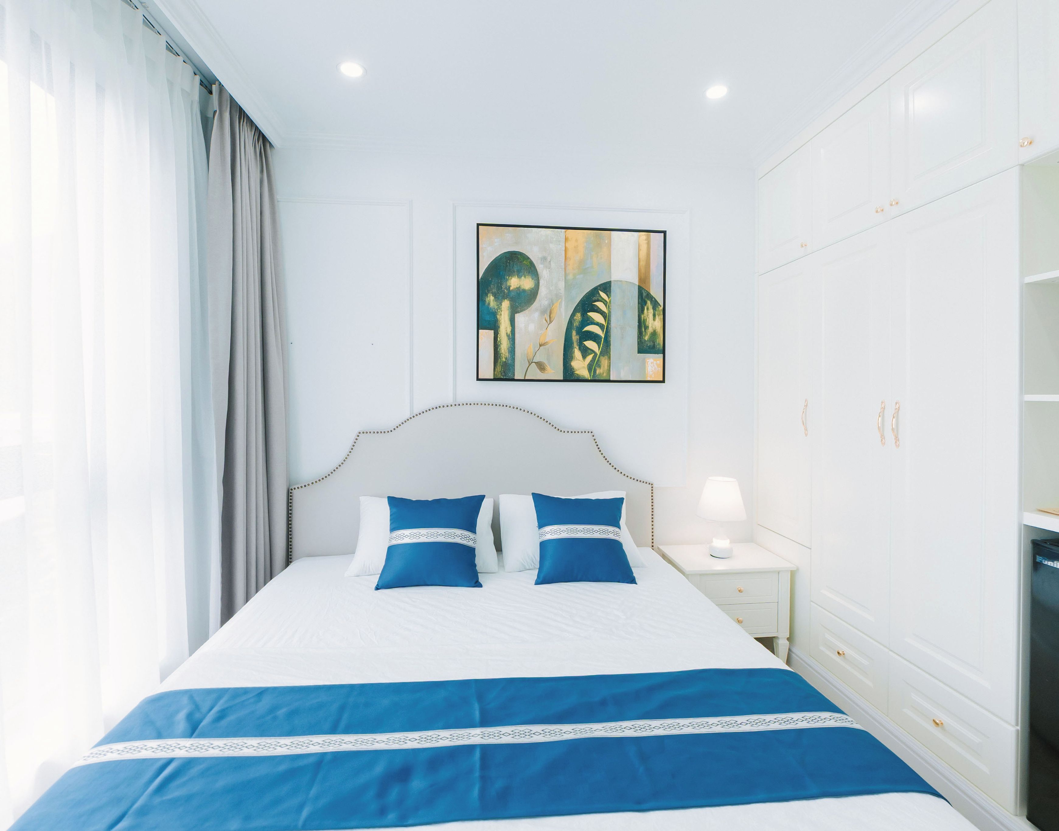 Habitación de hotel con cama, mesita de noche, una obra de arte en la pared y un minibar.