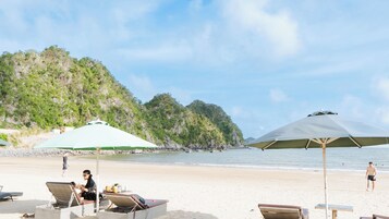 A beach with lounge chairs and umbrellas, a mountain in the background, and a logo for Latritcia Boutique Hotel.