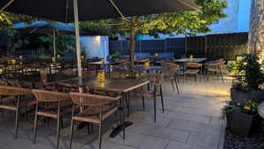 Un espace extérieur aménagé en terrasse, avec des tables et des chaises, entouré d’une clôture en bois et d’arbres.