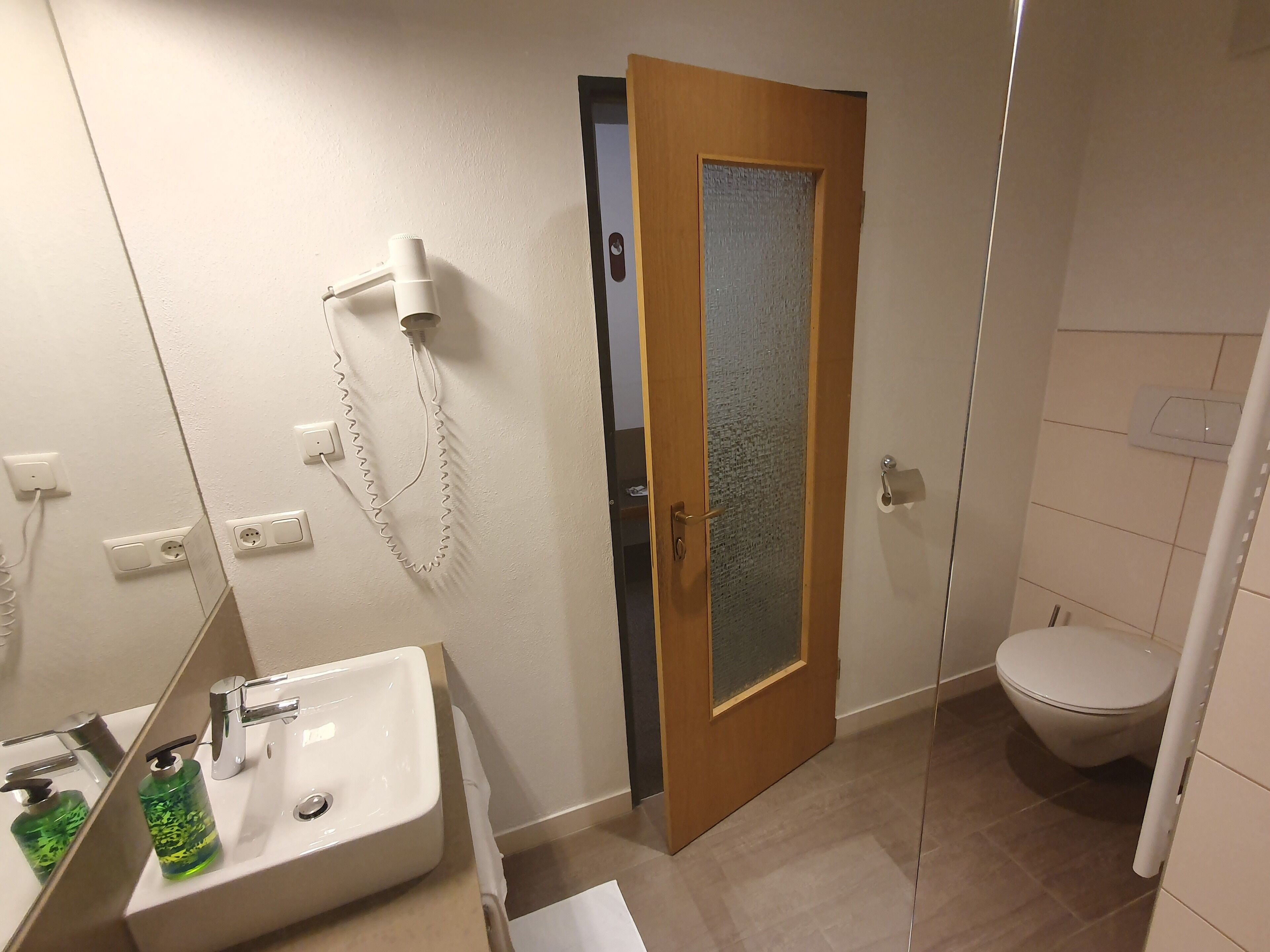 Une salle de bain équipée d’un lavabo, d’un sèche-cheveux, de toilettes et d’une porte en verre dépoli.