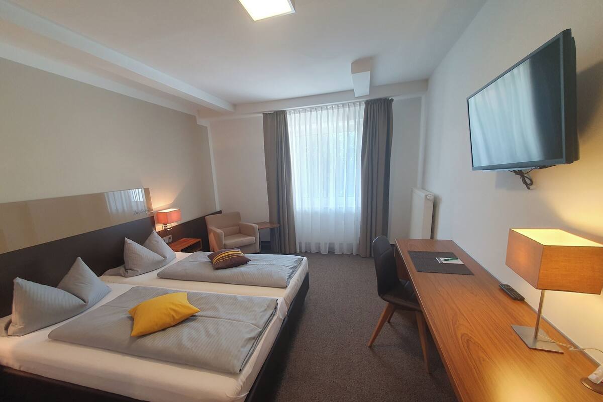 Hotelkamer met twee bedden, een bureau, een stoel, een televisie en een raam met gordijnen.