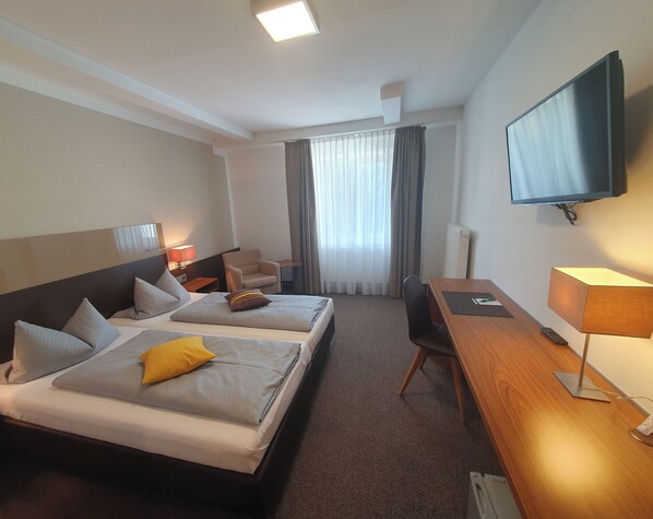 Une chambre d’hôtel avec deux lits, un bureau, une chaise, une télévision et une fenêtre avec des rideaux.