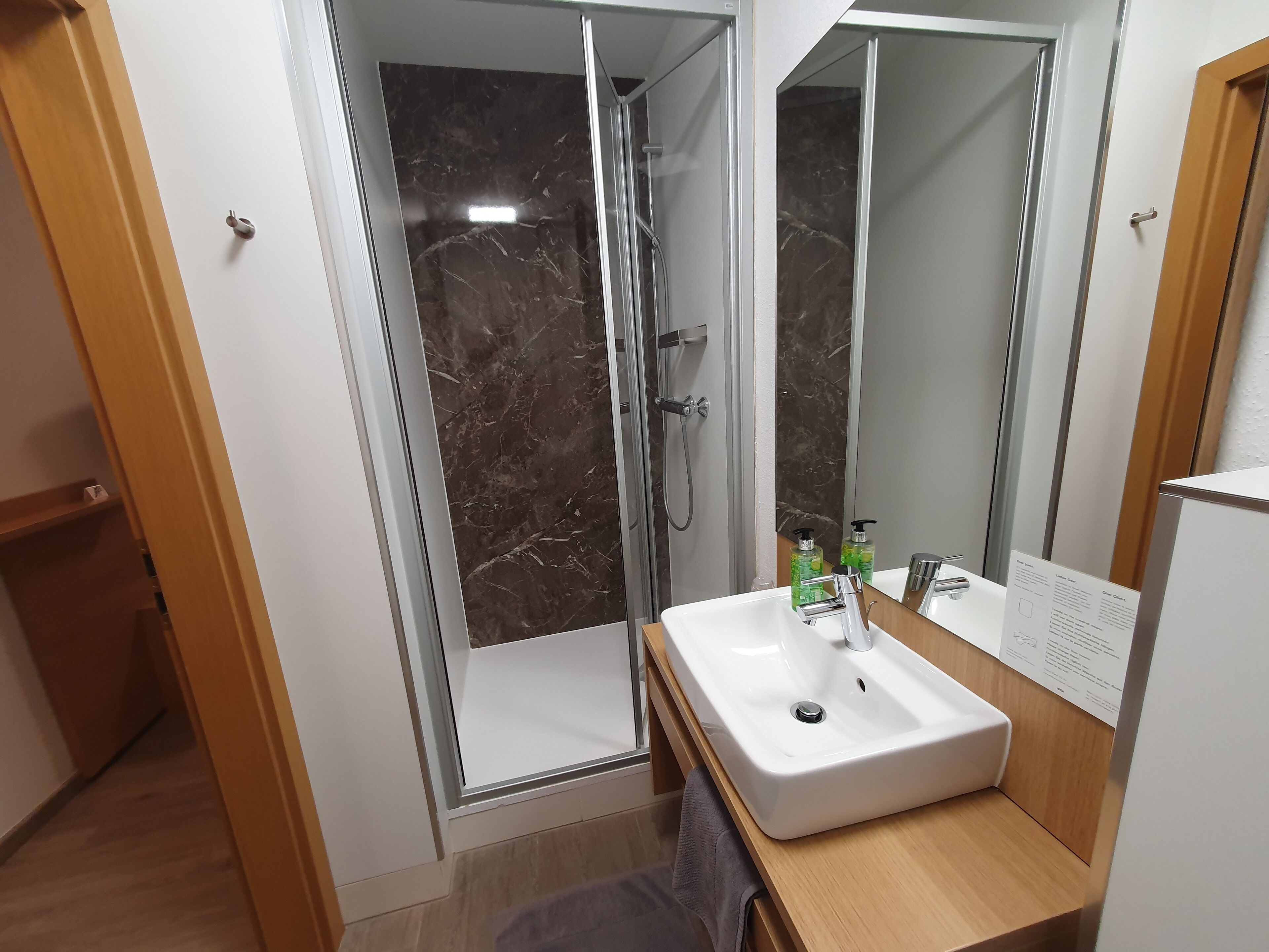 Een moderne badkamer met een douchecabine van glas, een witte wastafel en een grote spiegel.