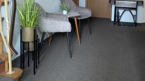 Un intérieur moderne comprenant un escalier, deux fauteuils confortables, une petite table, une plante en pot et un bureau agrémenté d’un vase de fleurs.