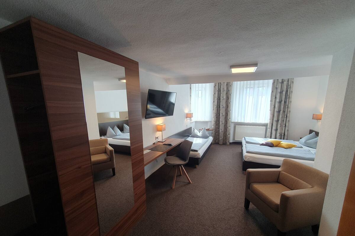 Een hotelkamer met een bed, een bureau, een stoel, een televisie en een grote spiegel.