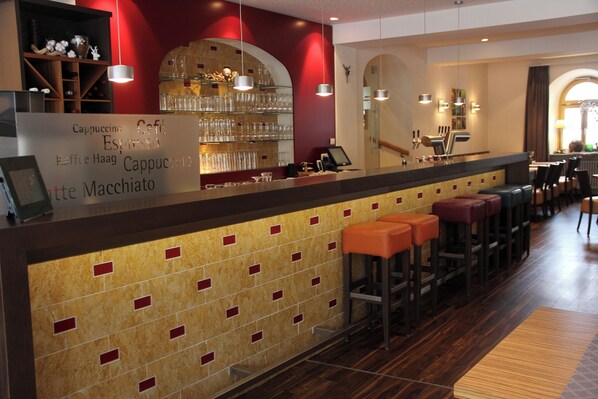 Zona de bar con pared de azulejos, taburetes y mostrador con una pizarra de menú.