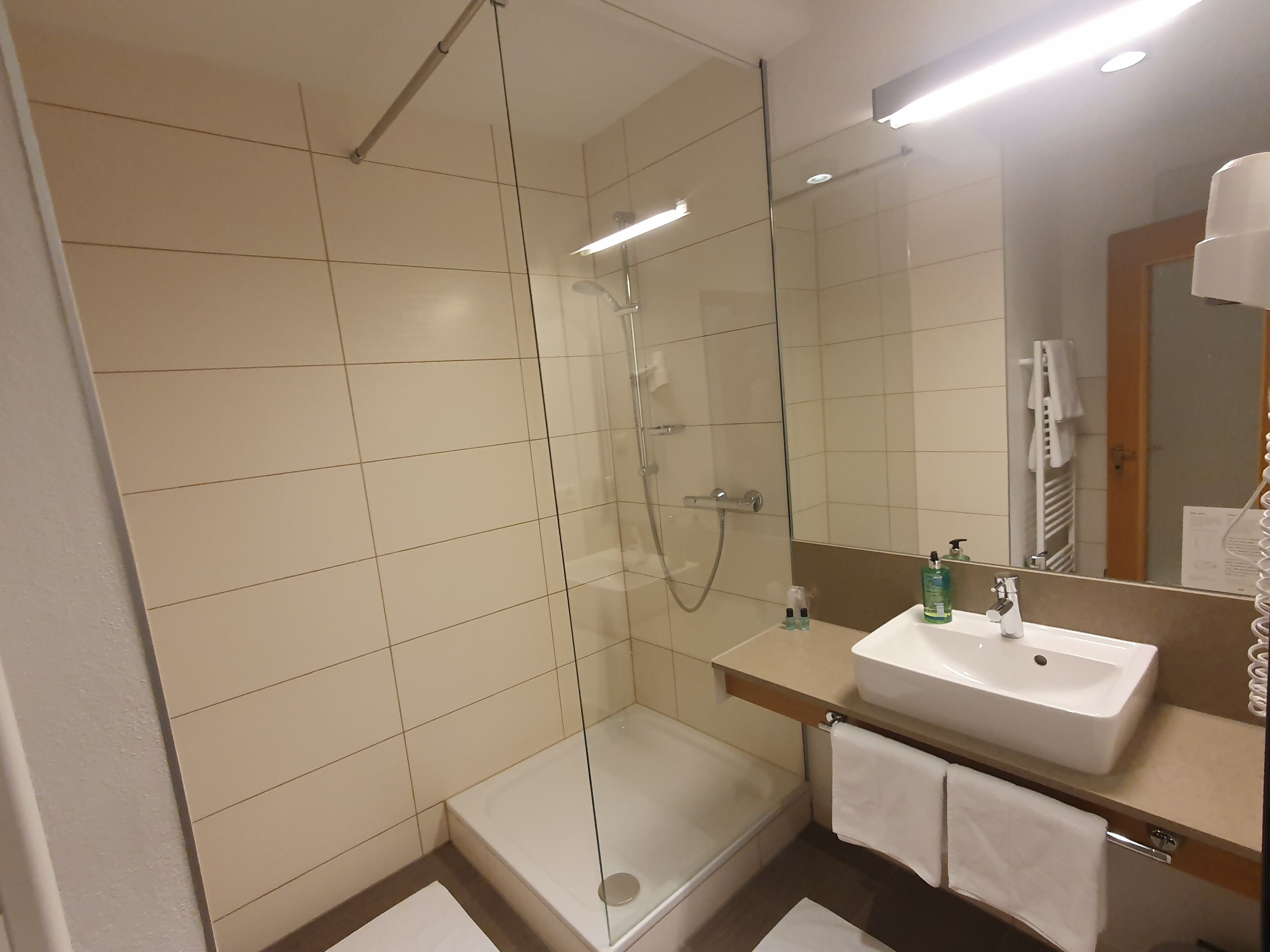 Un baño moderno con ducha de vidrio, lavamanos y espejo.
