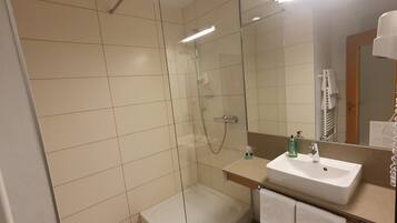 Un baño moderno con ducha de vidrio, lavamanos y espejo.