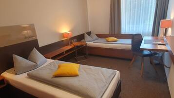A hotel room with two beds, a desk, a chair, and a lamp.